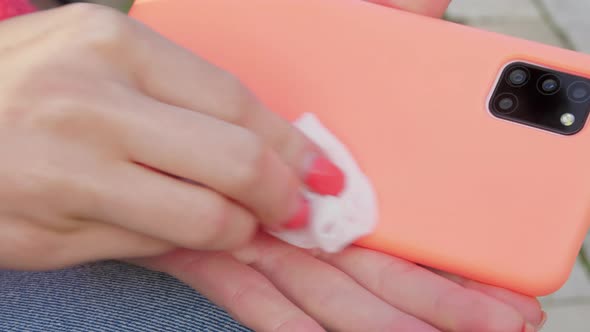 Lady Cleans Smartphone in Orange Case with Wet Wipe