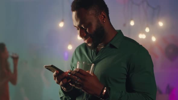 Glad Black Male Communicating Via Text Messages During Party