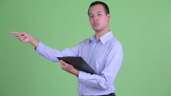 Happy Asian Businessman Talking While Holding Clipboard