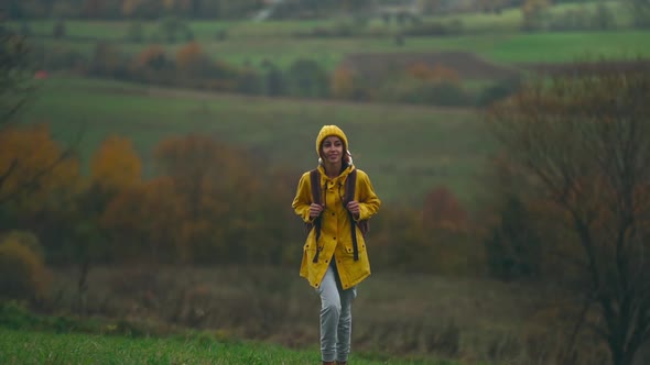 Slow Motion Inspired Young Pretty Woman Hiker in Yellow Raincoat with Backpack and Beanie Walking