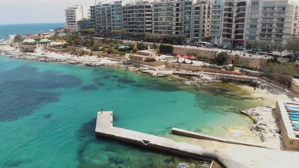 Pier over the warm Mediterranean sea on Sliema's seaside, in Malta - Slow Orbit aerial shot