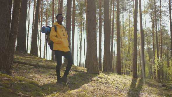 African Black Man Climbs Uphill in Woods in Yellow Jacket with Backpack in Slow Motion