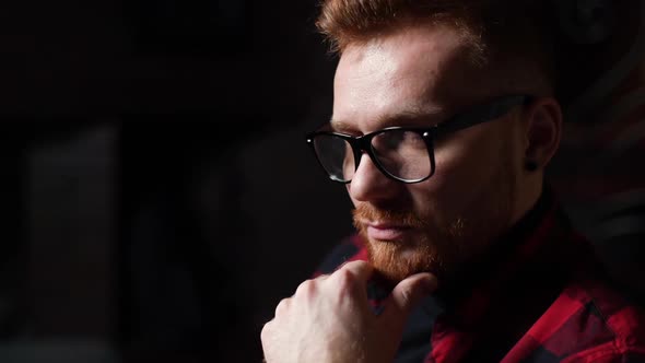 Closeup Face of Serious Beared Young Man Wearing Stylish Glasses Thoughtfully Holds Hand Near Chin