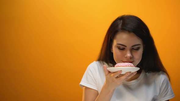 Happy Girl Smelling and Showing Donut to Camera, Sweetened Snack, Obesity Risk