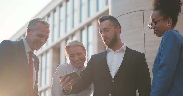 Diverse Colleagues Watching Content on Smartphone and Laughing Outdoors