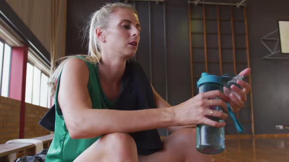 Caucasian female basketball player resting and drinking water