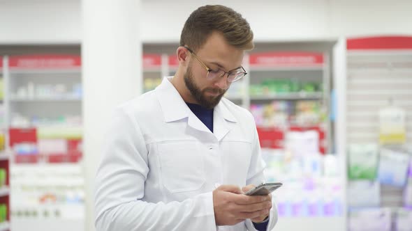 Young Caucasian Male Pharmacist Doctor in White Medical Uniform Using Smartphene