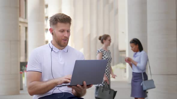 Young Caucasian Businessman Video Calling with Laptop While Sitting in City Outdoors