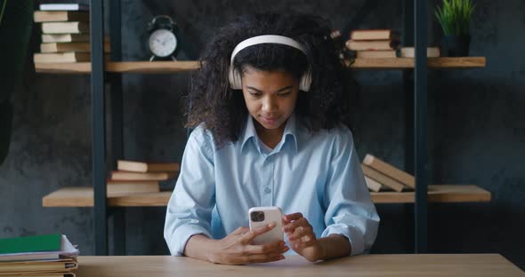 Cheerful African American Business Woman in Headphones Holding Smartphone Texting Message and