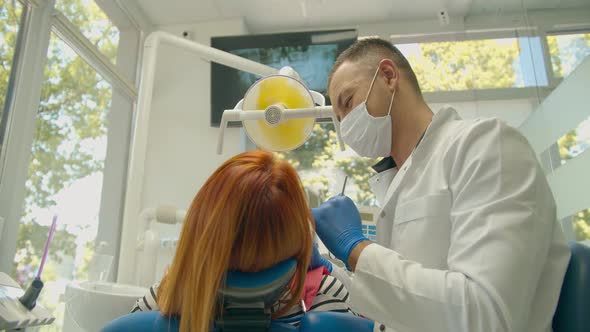 Professional Male Dentist Examines the Red-haired Girl Patient. Shooting From Behind View, Caucasian