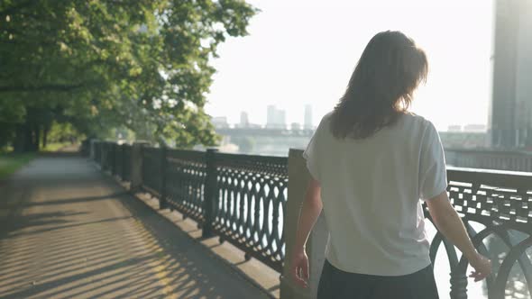 Woman is Walking Alone on River Embankment in City Center Admiring Modern Skyscrapers in Downtown