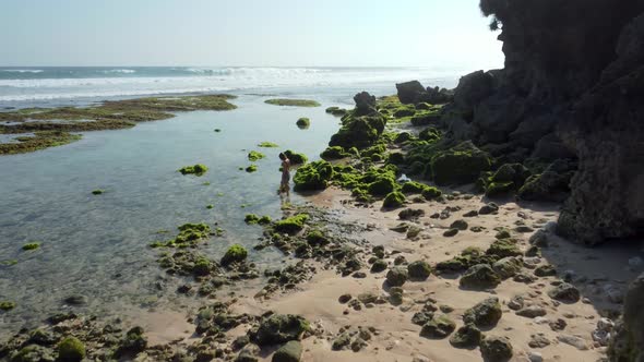 Woman walks in the beach near to rocks seaweed