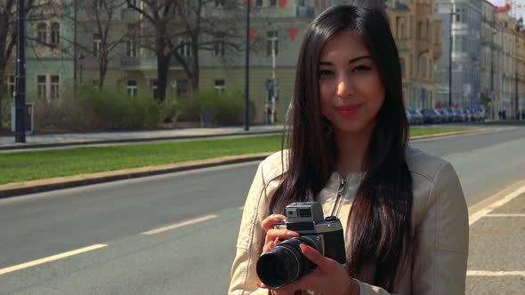 A Young Asian Woman Takes a Picture of the Camera with Her Own Camera and Smiles - an Urban Area