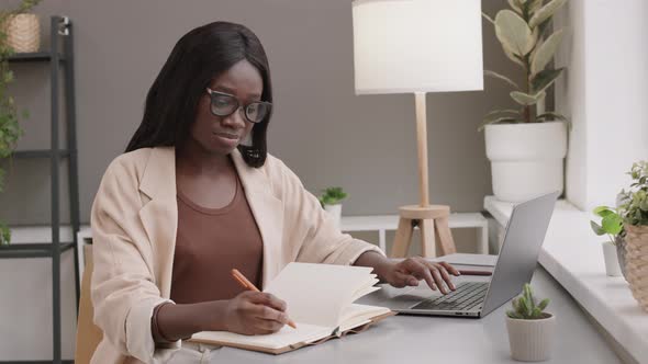 African Businesswoman Using Laptop and Writing in Notepad