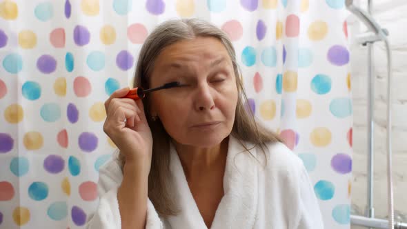 Portrait of Senior Woman Putting Mascara Standing in Bathroom in Morning