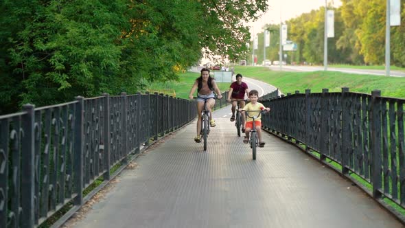 Fit family riding bicycles and crossing metal bridge