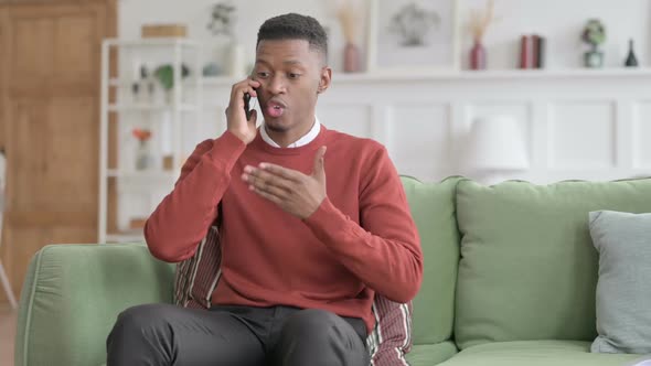 Angry African Man Talking on Phone on Sofa