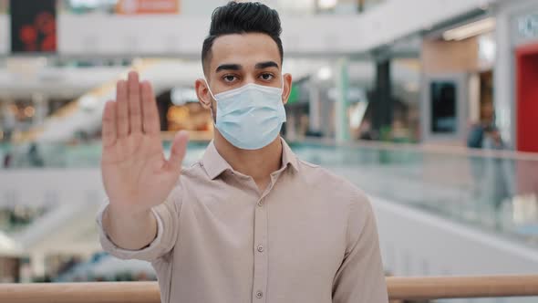 Portrait of Young Hispanic Man Wearing Medical Mask Put Palm Forward Serious Arab Guy Looking at