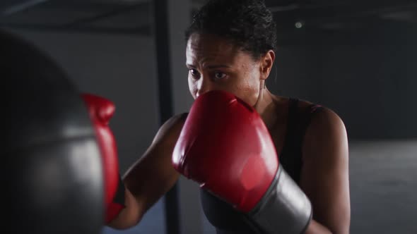 African american woman wearing boxing gloves training in empty building punching punchbag
