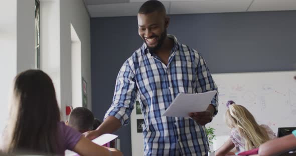 Video of happy african american male teacher giving test an clapping hands with caucasian girl