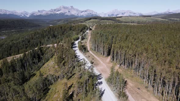 A car driving along a dusty logging road through vast coniferous forests on a sunny day in the Rocki