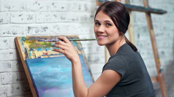 Attractive Female Painter Posing at Workshop Holding Paintbrush During Drawing Picture