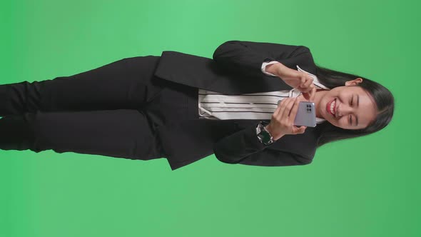 A Smiling Asian Business Woman Using Mobile Phone While Walking Through Green Screen In The Studio