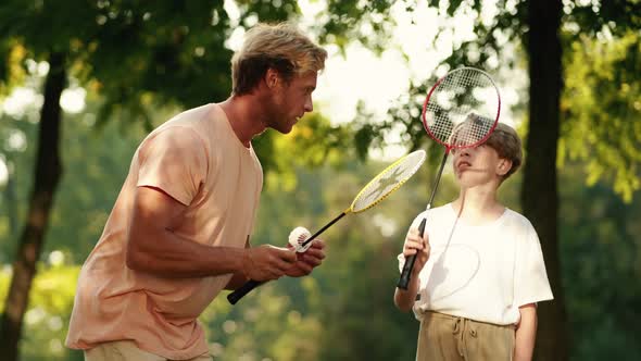 A cheerful father is teaching his son playing badminton