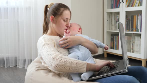 Young Mother Stroking Her Baby While Working From Home Office on Laptop