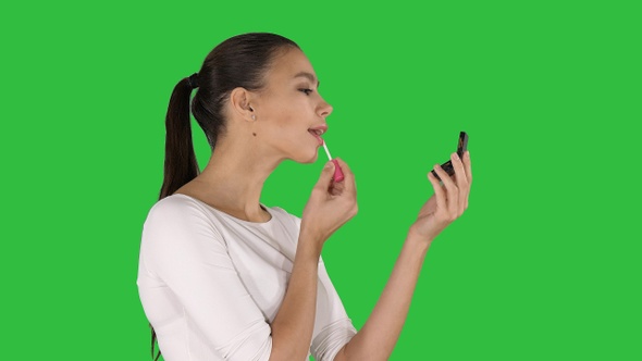 Beautiful young woman putting on lipstick on a Green Screen