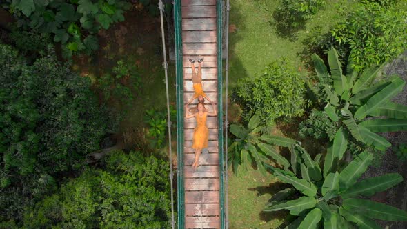 Aerial Shot of a Young Woman and Her Little Son Laying on a Suspension Bridge Over the Jungles