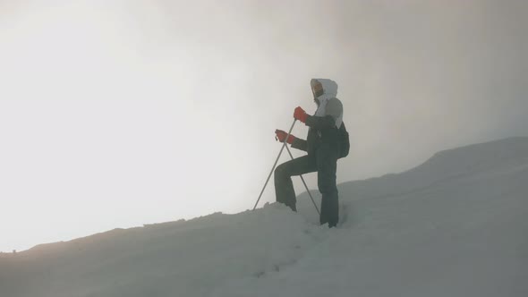 A Young Woman is Standing on the Slope of a Snowcovered Mountain and Taking a Break