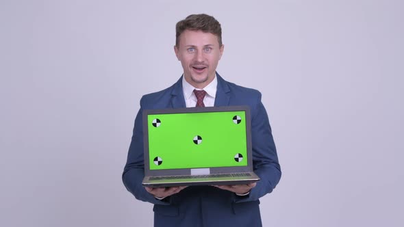 Happy Bearded Businessman Showing Laptop and Looking Surprised