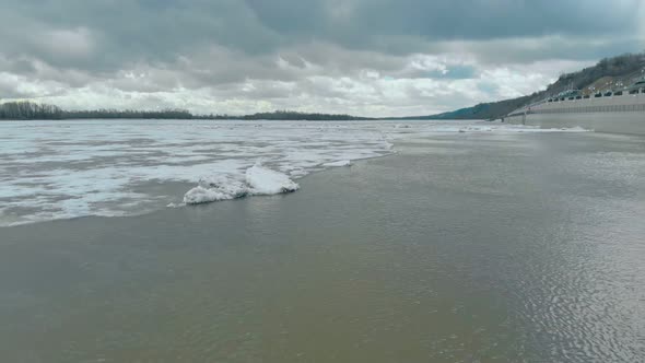 Wide River with White Ice Surrounded By Dense Hilly Forests