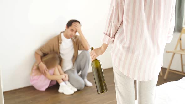 Closeup Woman's Hand with an Empty Bottle Against the Background of a Despresicive Husband and