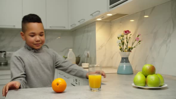 Cheerful Black Boy Choosing Between Orange and Glass of Juice Indoors