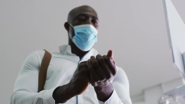 African american businessman in face mask disinfecting hands in office