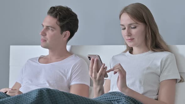 Disappointed Man Sitting with Couple While She Uses Smartphone