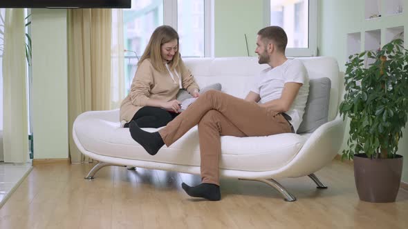 Wide Shot Portrait of Happy Relaxed Caucasian Man and Woman Sitting on Couch Talking and Laughing