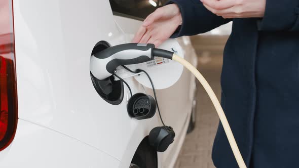Womans Hand Unplugging an Electric Car After Charging in the Parking