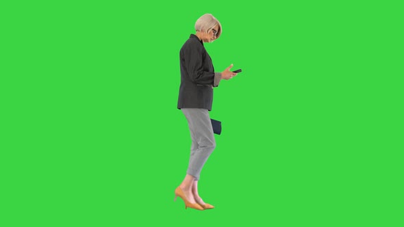 Elegant Senior Woman Using Smartphone While Walking on a Green Screen, Chroma Key.