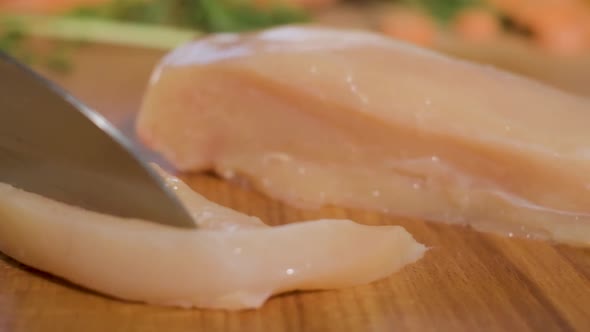 Knife Slicing Chicken Breast Fillet On Wooden Chopping Board. - close up, slow motion