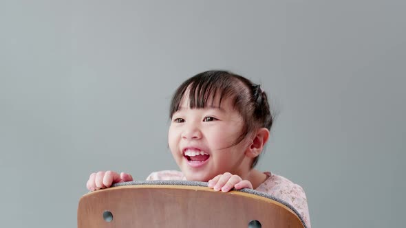 Cute Asian girl in dress enjoy playing peek a boo on a chair, smiling and laughing with happiness in