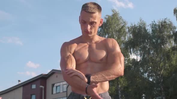 Muscular athletic young man rubs oil all over the body