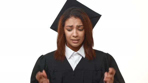 Stressed Young African American Graduate in Black Robe and Square Academical Cap Crossing Her