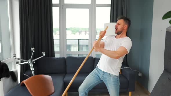 Man Fooling Around While Cleaning the House and Singing Into a Mop Instead of a Microphone