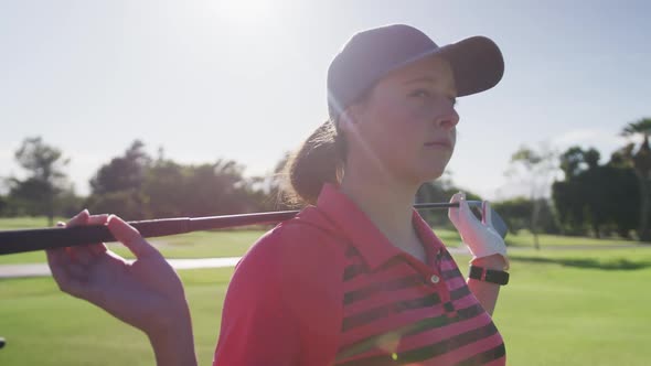 Portrait of female caucasian golf player smiling while standing with golf club around her back at go