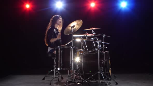 Girl Drummer with Chopsticks Beats Rhythmic Music, Black Background, Red Light Blue, Side View