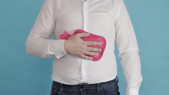 A Man in a White Shirt Puts a Red Heating Pad on His Stomach