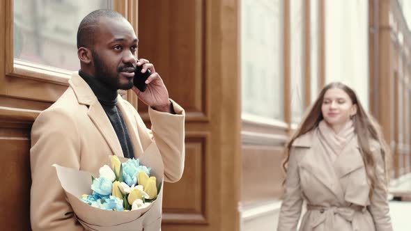 African American Man with Flowers Talking By Phone and Waiting for His Girlfriend